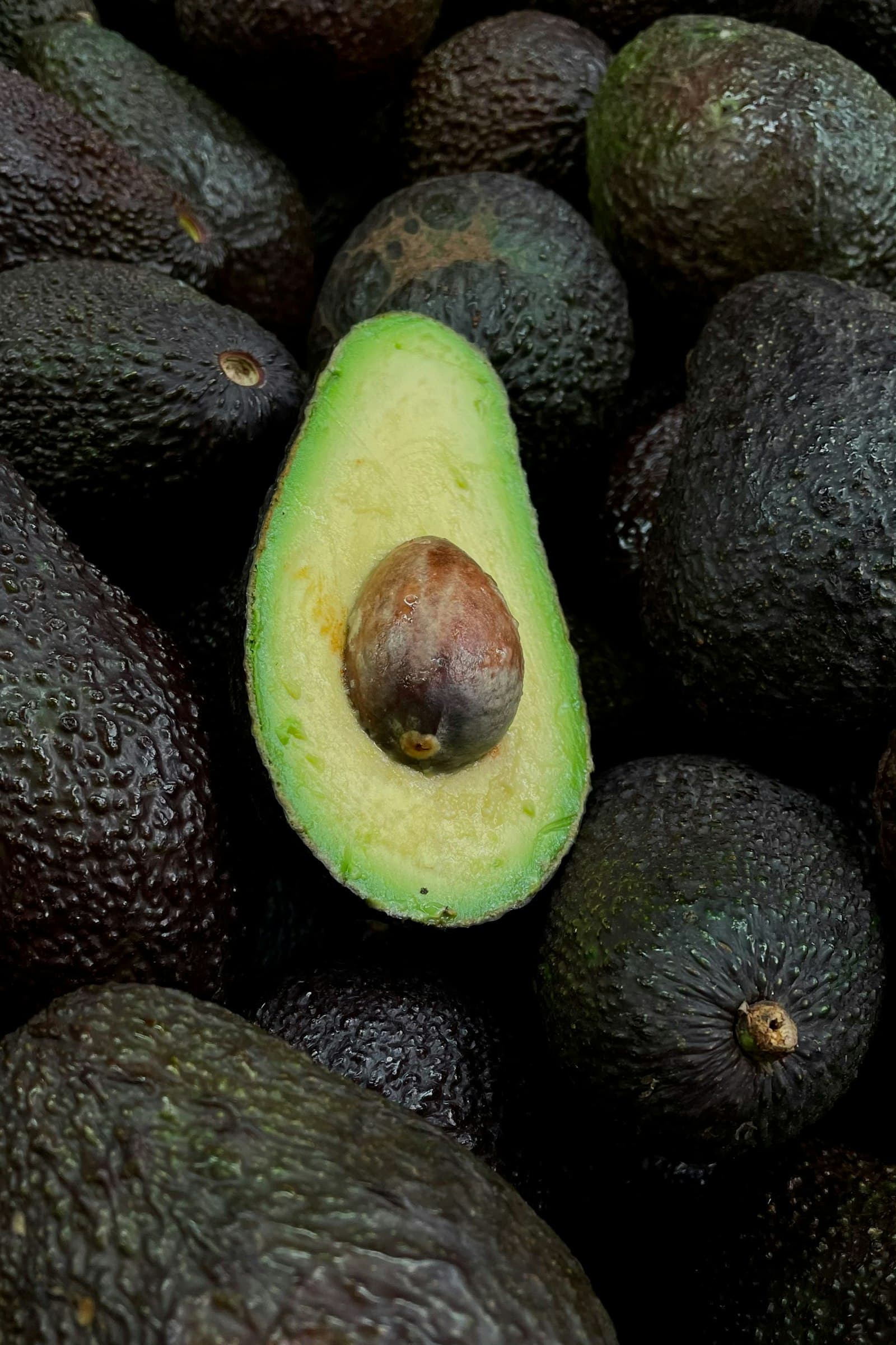 Whole and halved avocados against a dark background