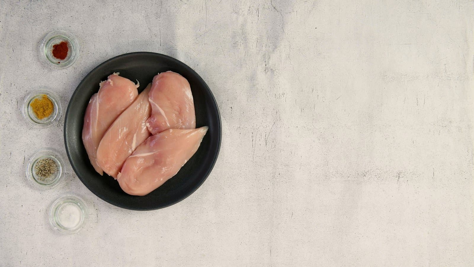 Two raw chicken breasts in a dark bowl